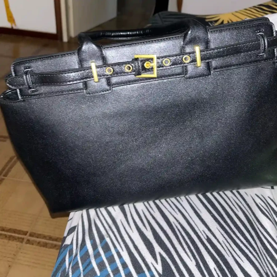 Svart handväska i glänsande finish. Med guldspänne och elegant form är den ett perfekt val för dig som söker sofistikerad och rymlig väska.